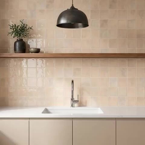 Minimalist kitchen walkthrough with beige glossy square wall tiles, white quartz countertop, and taupe laminate cabinets