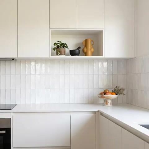 Minimalist kitchen walkthrough with frosty white laminate cabinets and vertical white subway backsplash tile